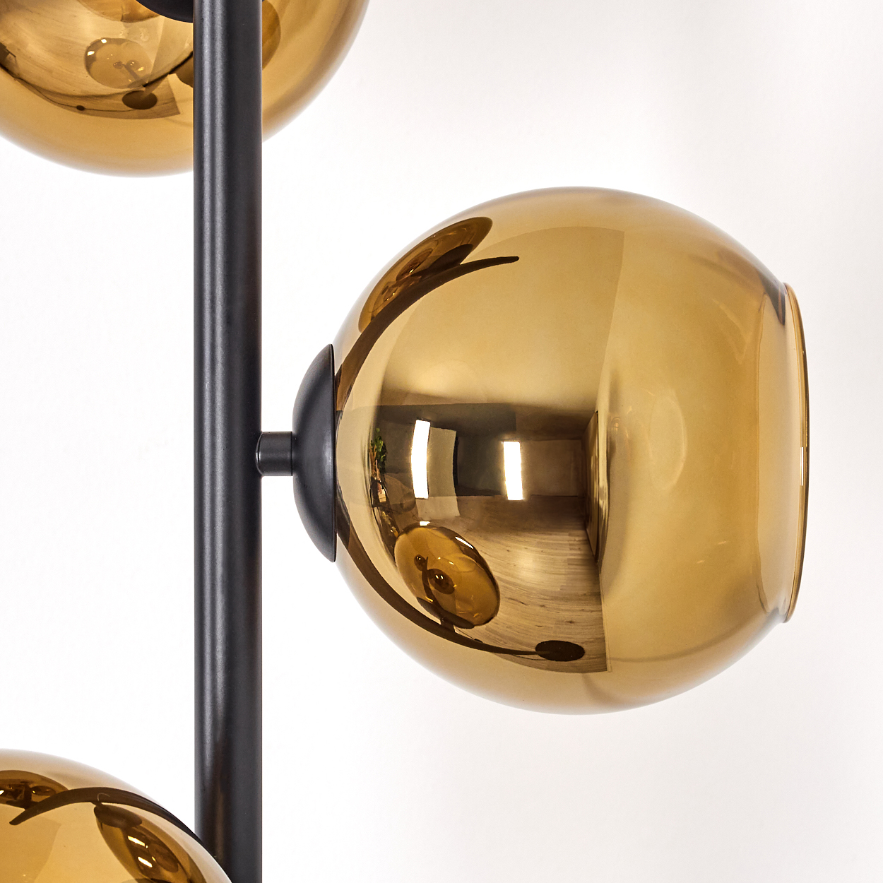 Eine moderne Lampe mit drei bernsteinfarbenen Glaskugeln an einer schwarzen Metallstange vor weißem Hintergrund.