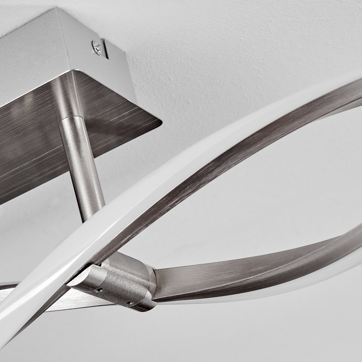 Eine moderne Deckenleuchte. Sie hat gebogene, metallische Arme mit weißen, leuchtenden Elementen, montiert auf einem gebürsteten Metallsockel.