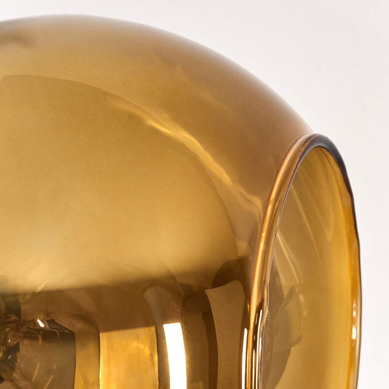 Nahaufnahme einer goldenen Glaslampe. Das Licht reflektiert auf der abgerundeten Oberfläche, mit dunklem Rand und weißem Hintergrund.