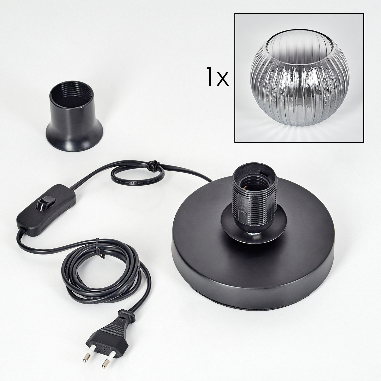 Schwarze Lampenteile: Sockel, Fassung, Schalter, Kabel, Stecker. Glaslampenschirm oben rechts. Alles auf weißer Oberfläche.