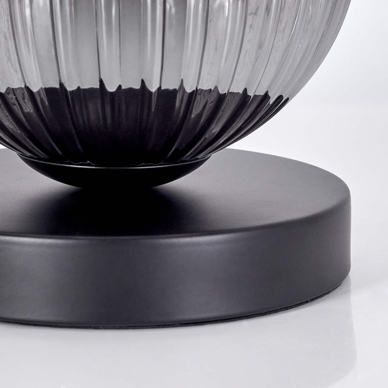 Nahaufnahme einer dekorativen Lampe. Sie hat eine gerippte, dunkelgraue Glasschale auf einem schwarzen, kreisförmigen Sockel.