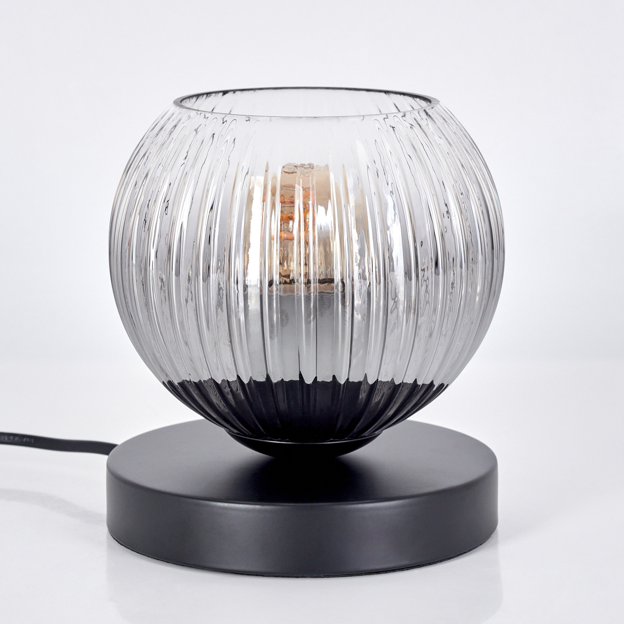 Eine dekorative Lampe mit geripptem, grauem Glaskugelschirm und schwarzem Sockel. Eine Glühbirne ist im Schirm zu sehen.