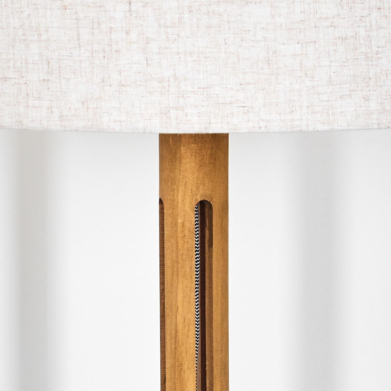Nahaufnahme einer Lampe. Die Lampe hat einen beigefarbenen Lampenschirm und einen Holzsockel. Ein schwarz-weißes Kabel ist sichtbar.