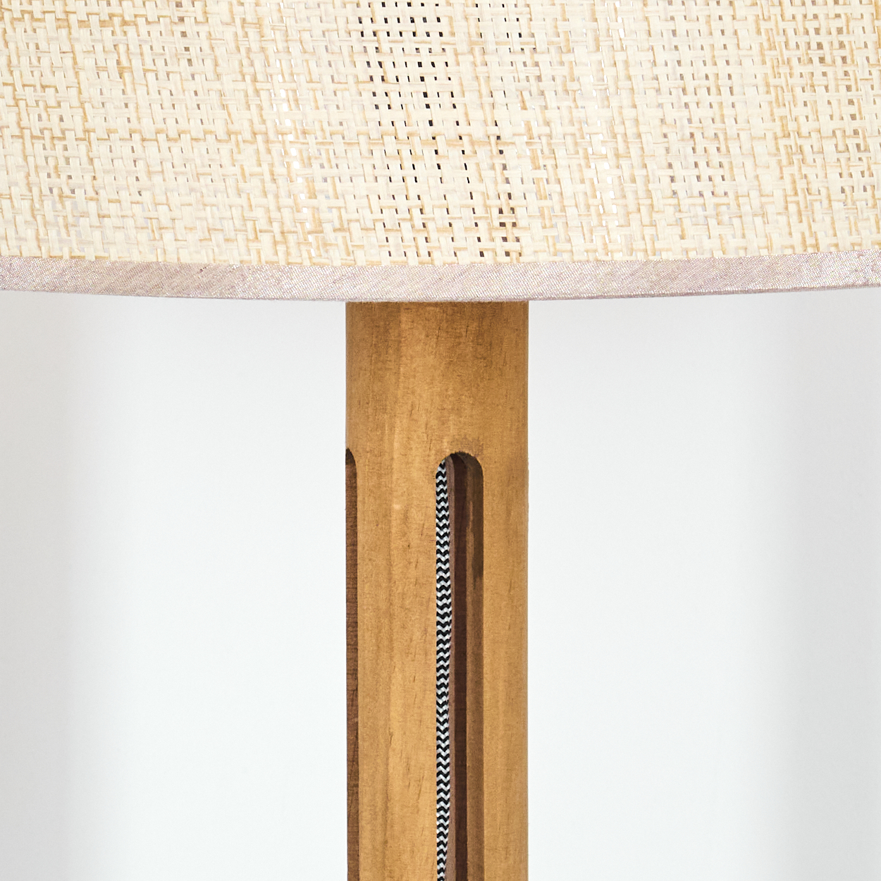 Nahaufnahme einer Lampe. Der Lampenschirm ist gewebt und beige, der Holzsockel hat ein schwarz-weißes Kabel.