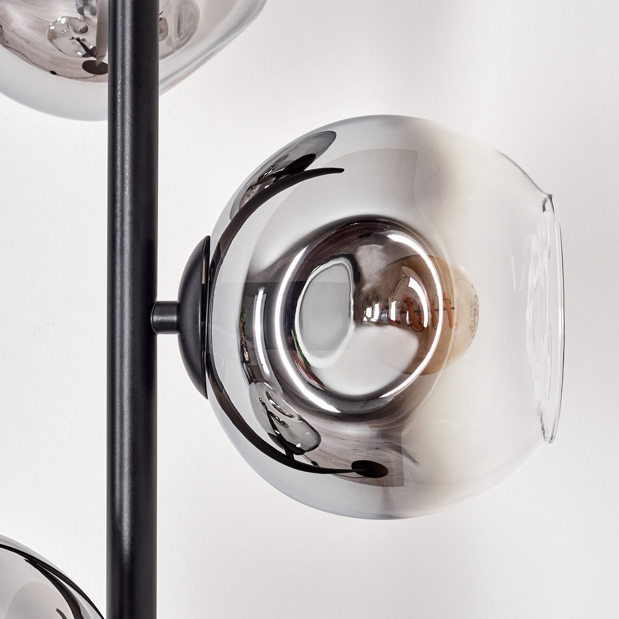 Nahaufnahme einer modernen Lampe mit drei Glaskugeln. Die Kugeln sind reflektierend. Ein schwarzer Metallpfosten trägt die Kugeln vor weißem Hintergrund.