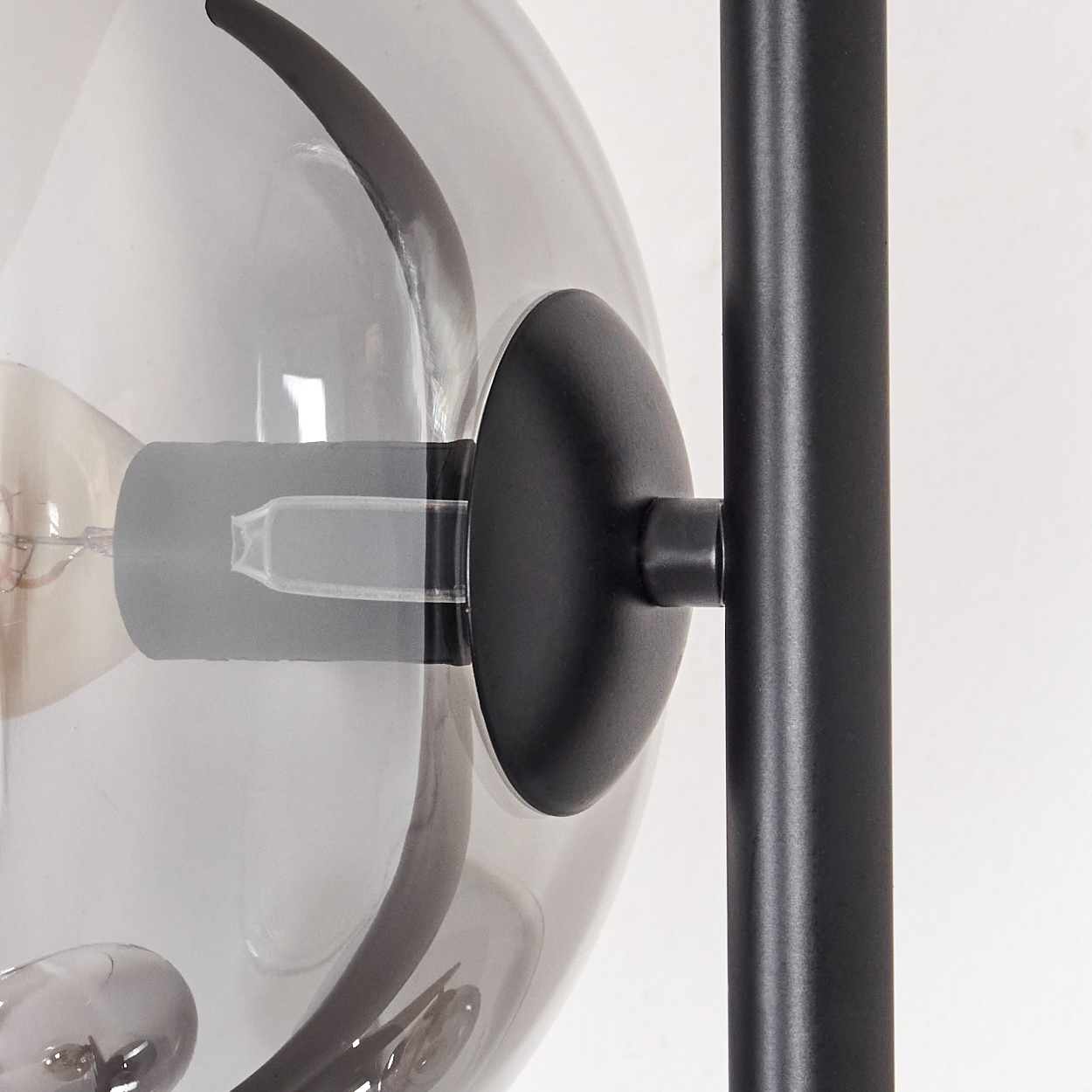 Nahaufnahme einer modernen Lampe. Eine graue Glaskugel mit einer Glühbirne im Inneren ist an einem schwarzen Metallrahmen befestigt.