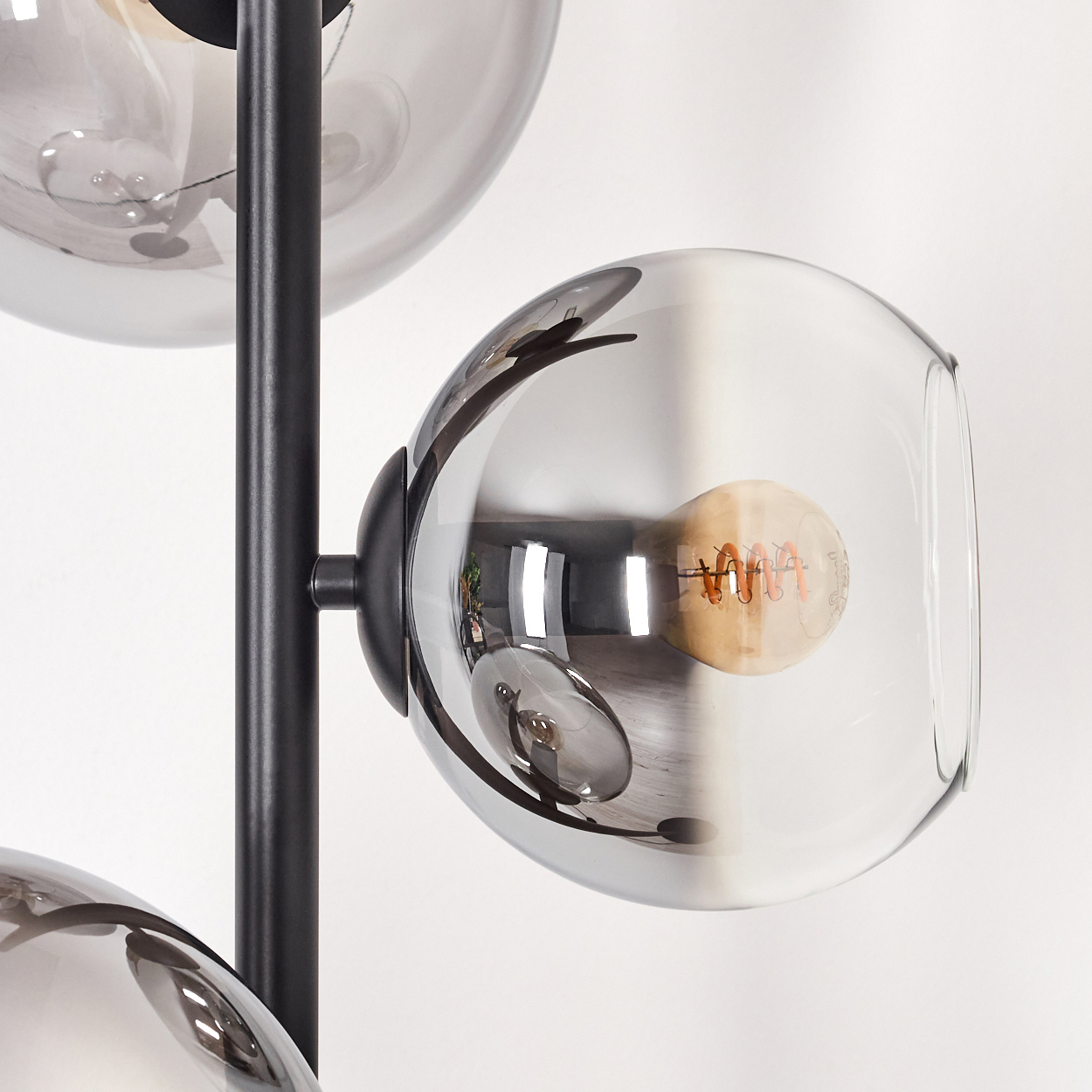 Nahaufnahme einer modernen Lampe mit drei grauen Glaskugeln. Jede Kugel hat eine Glühbirne. Die Lampe hat einen schwarzen Metallrahmen.