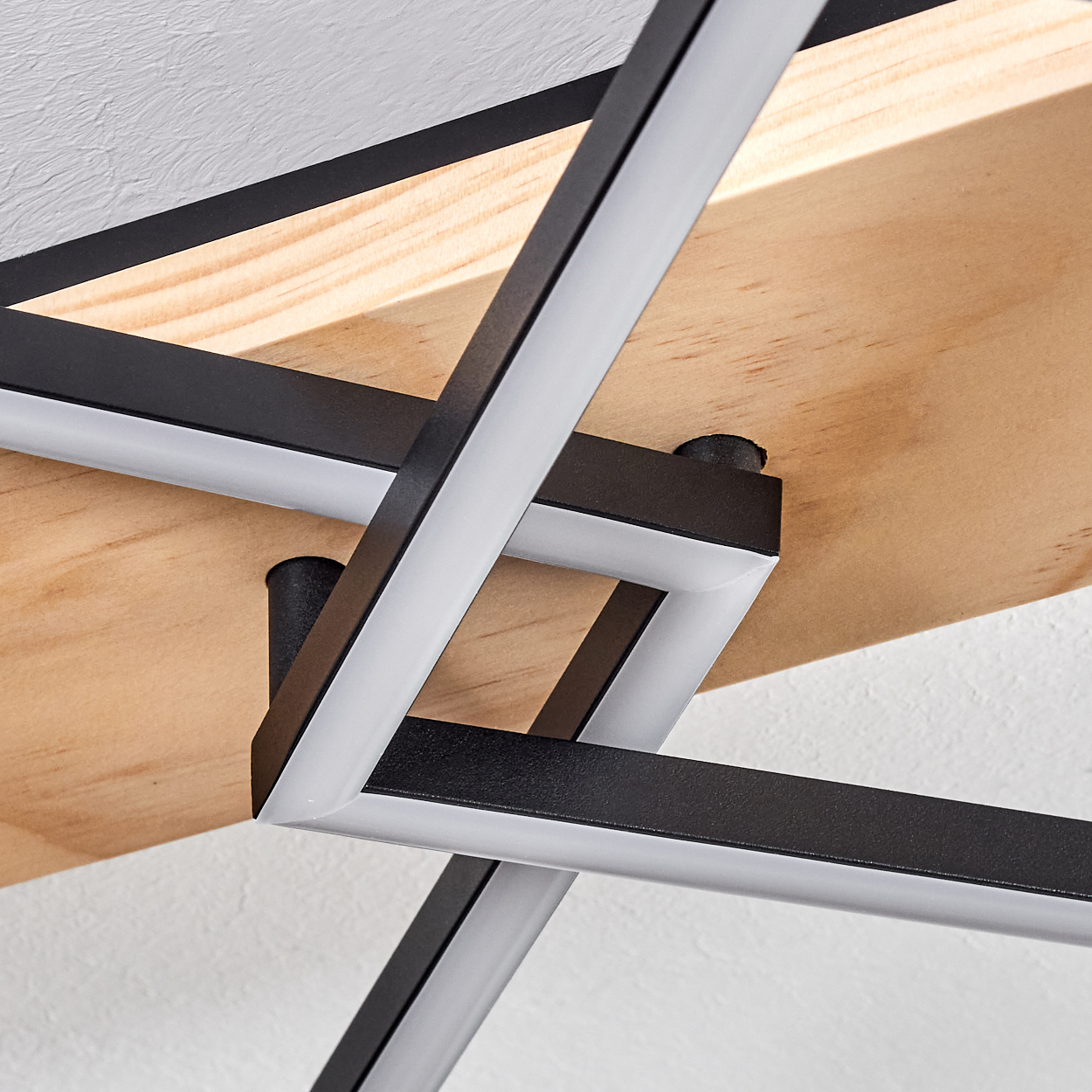 Geometrische schwarz-weiße Leuchte vor einer hellen Holzplatte, montiert an einer weißen strukturierten Decke. Abstraktes Design.