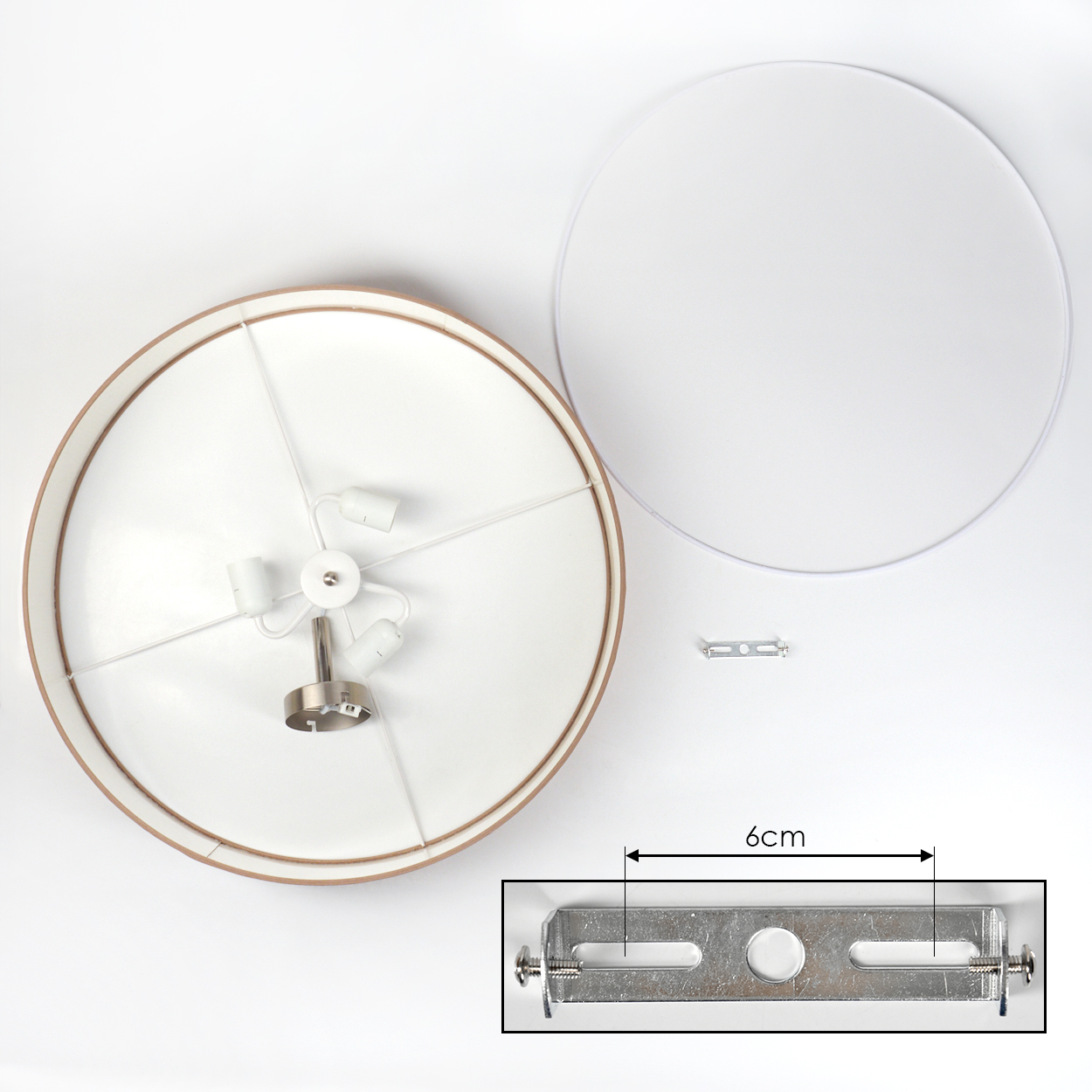 Draufsicht einer zerlegten Lampe. Zu den Komponenten gehören ein weißer Lampenschirm, eine Metallhalterung und ein kreisförmiger Rahmen.