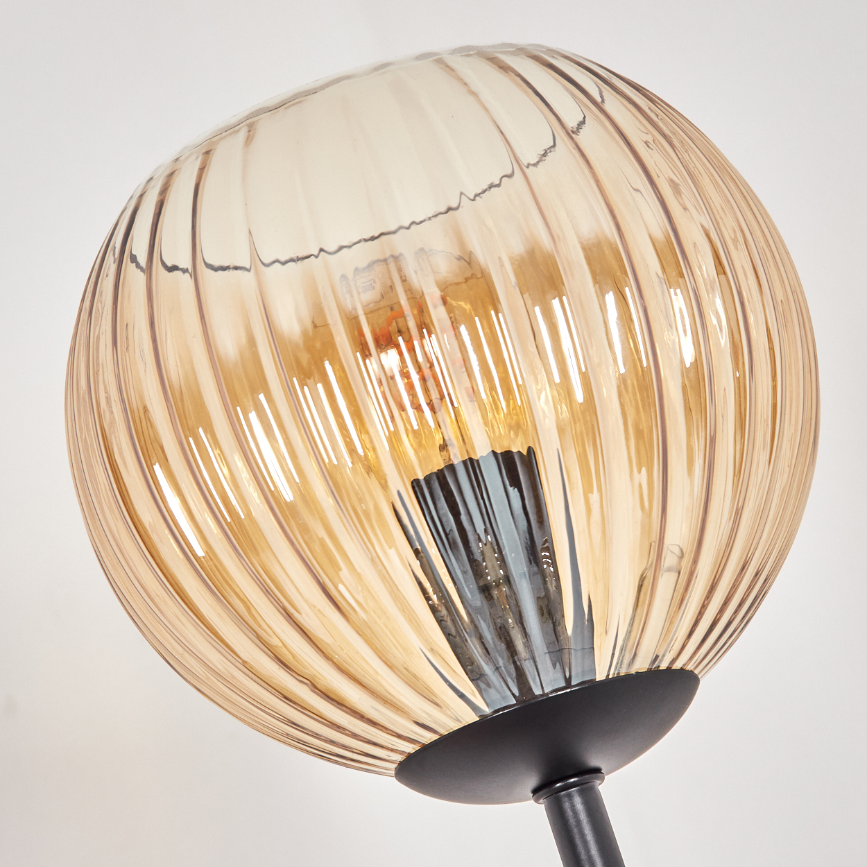 Nahaufnahme einer Lampe mit rundem, geripptem, bernsteinfarbenem Glasschirm. Ein schwarzer Sockel und Stiel tragen den Schirm vor weißem Hintergrund.