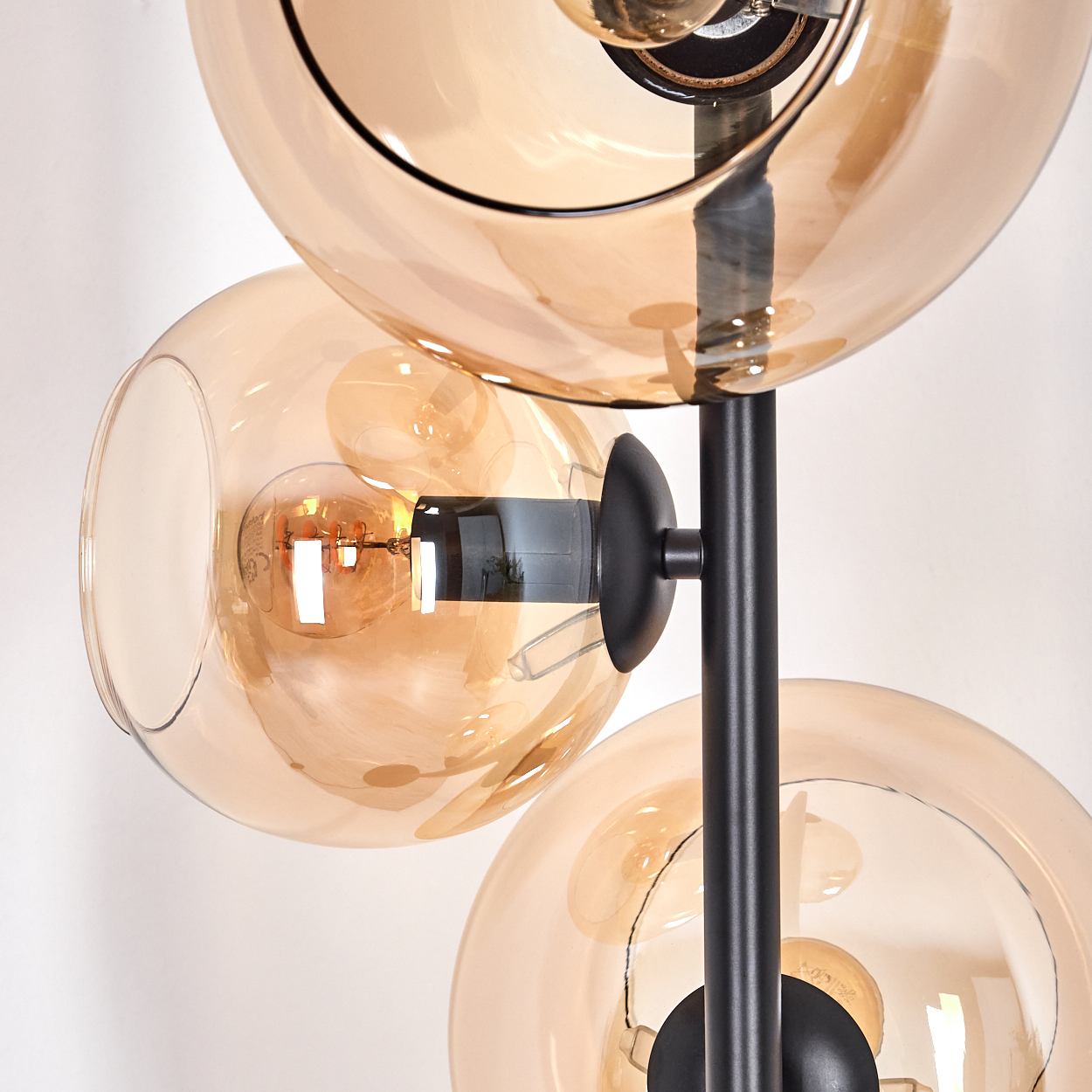 Nahaufnahme einer modernen Lampe mit drei bernsteinfarbenen Glaskugeln und schwarzem Metallträger, beleuchteten Glühbirnen innen. Weißer Hintergrund.