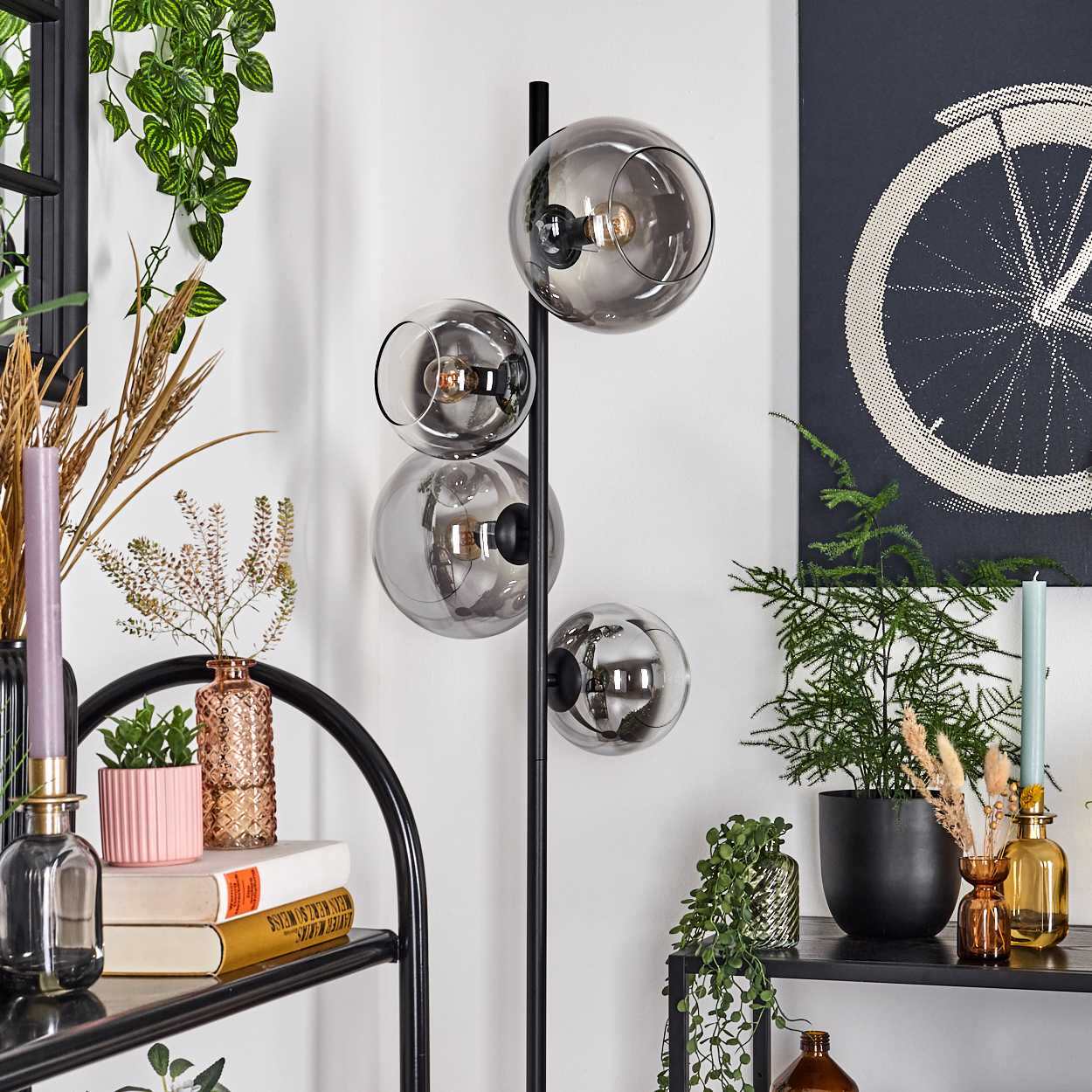 Ein modernes Interieur mit einer schwarzen Lampe mit vier Glaskugeln, Pflanzen, Büchern und einem Fahrradrad-Poster.