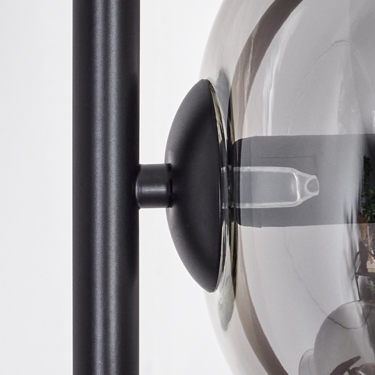 Nahaufnahme einer schwarzen Lampenstange mit einem rauchigen Glasschirm. Der Schirm hat eine Glühbirne, der Hintergrund ist weiß.