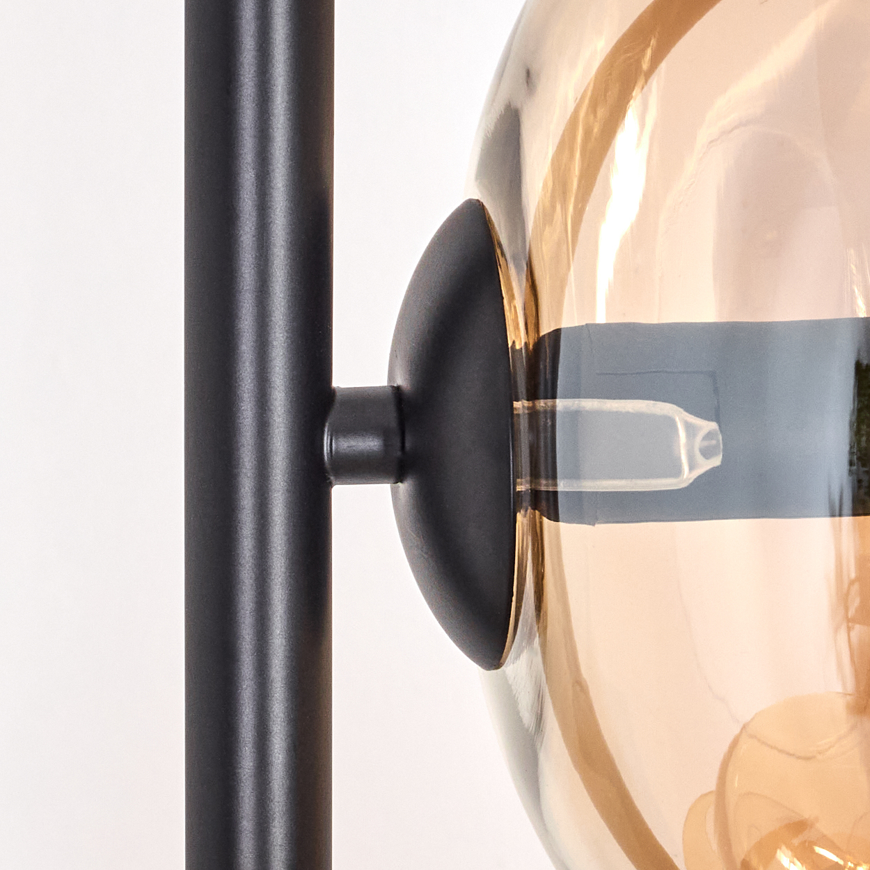 Nahaufnahme einer Lampe. Sie hat einen schwarzen Metallrahmen und einen runden, bernsteinfarbenen Glasschirm. Im Schirm ist eine Glühbirne sichtbar.