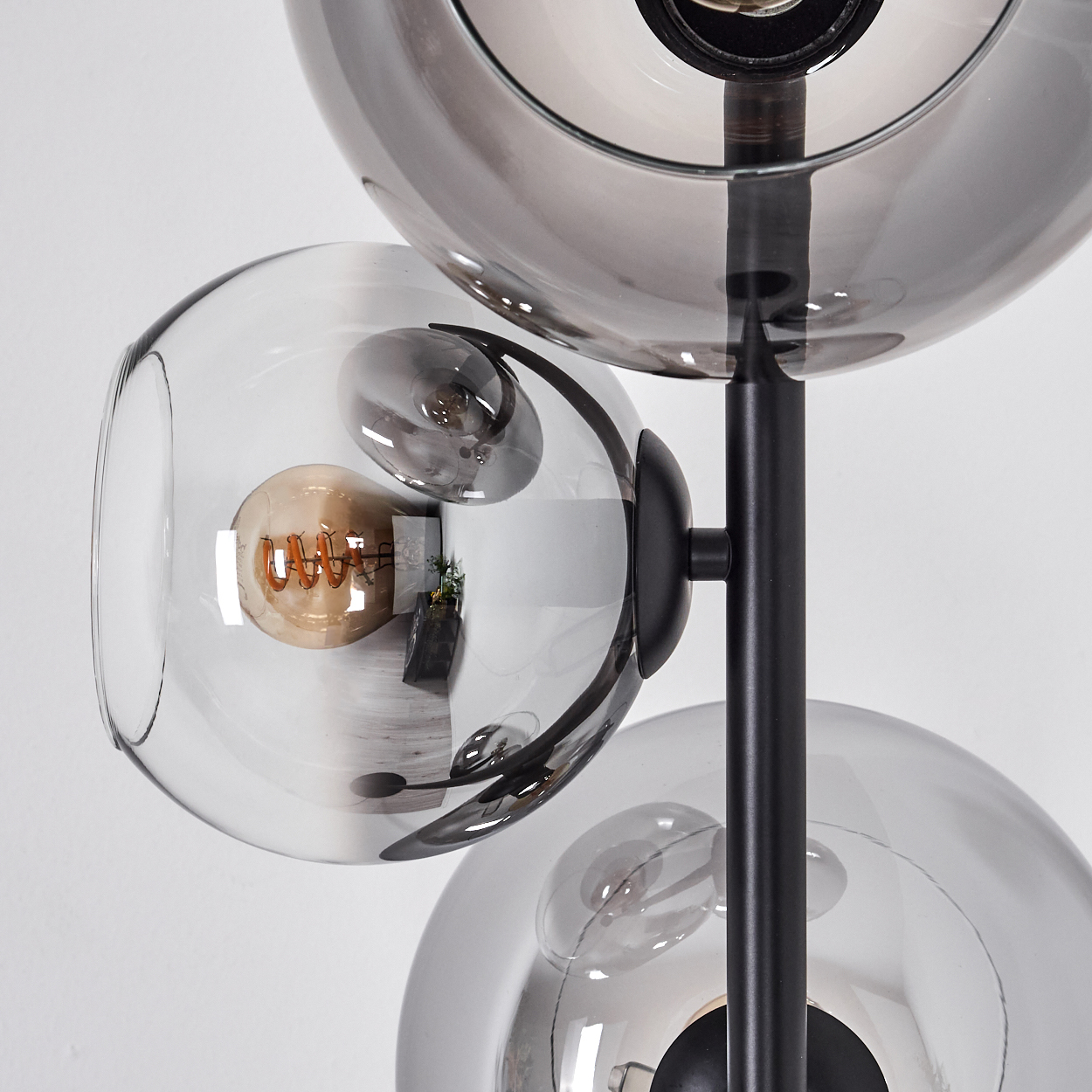 Nahaufnahme einer modernen Lampe mit drei Glaskugeln. Jede Kugel hat eine Glühbirne. Die Lampe ist schwarz mit weißem Hintergrund.