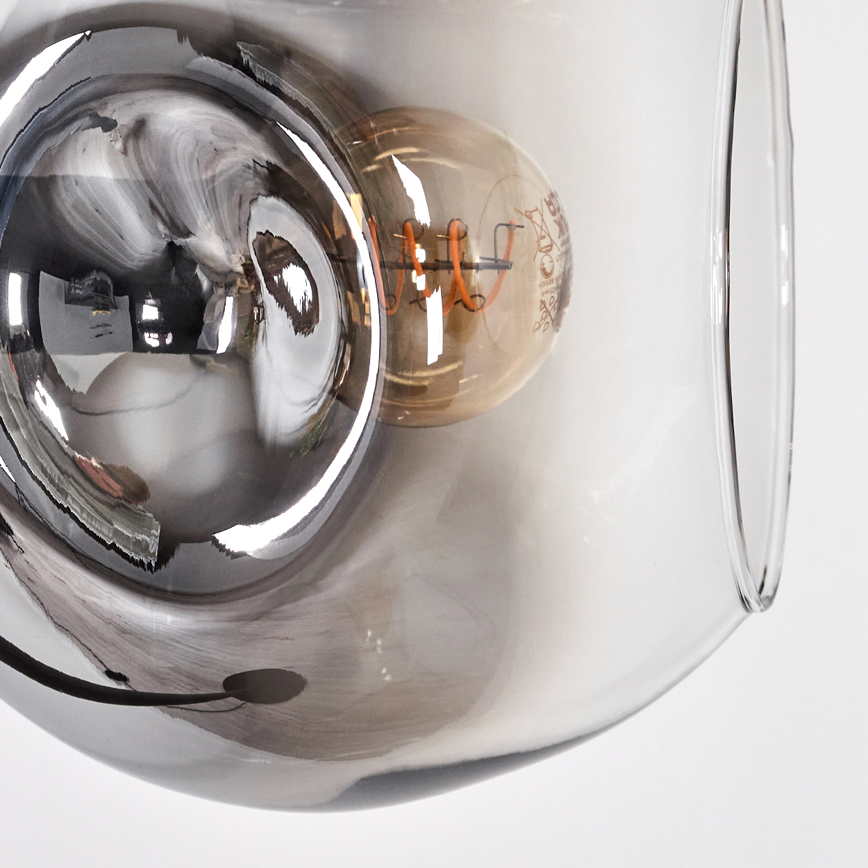 Nahaufnahme einer Glasleuchte mit einer Glühbirne. Das Glas ist klar und getönt und reflektiert die Umgebung.