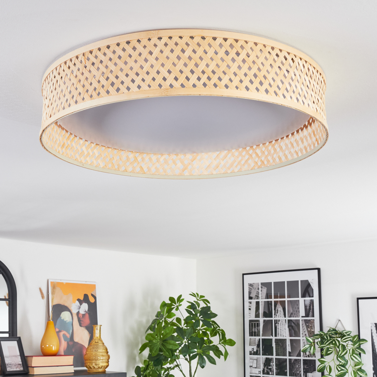 Eine Deckenlampe aus gewebtem Bambus. Die Lampe ist kreisförmig, mit einem gewebten Schirm und einem weißen Innenraum. Weitere Raumdekorationen sind sichtbar.