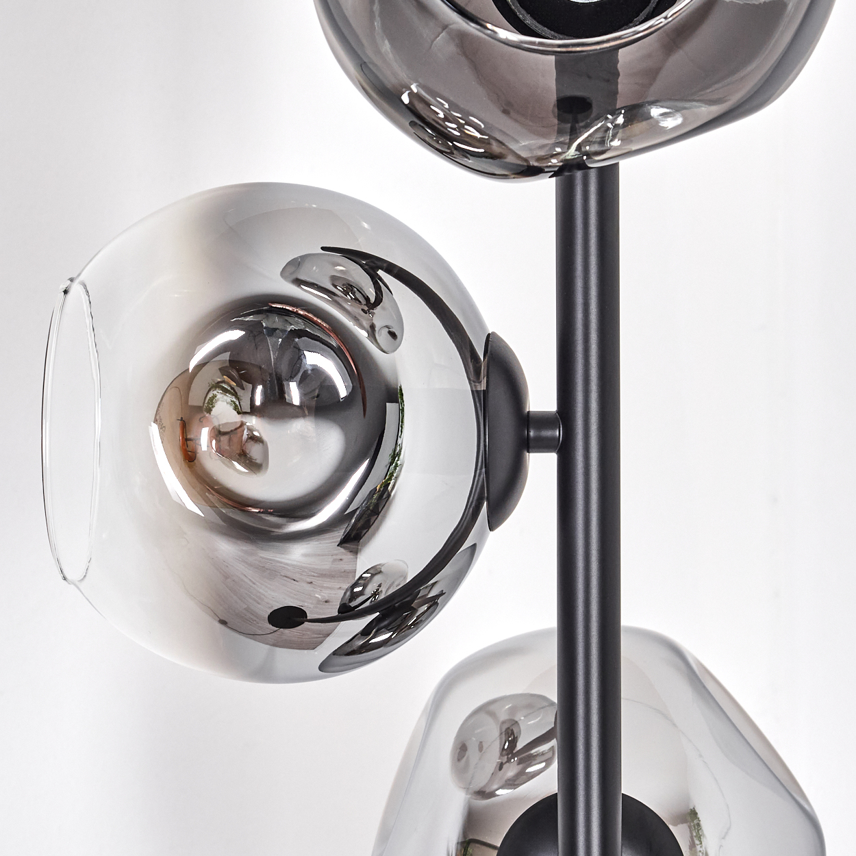 Eine moderne Lampe mit drei grauen Glaskugeln, die die Umgebung reflektieren, an einer schwarzen Metallsäule vor weißem Hintergrund befestigt.