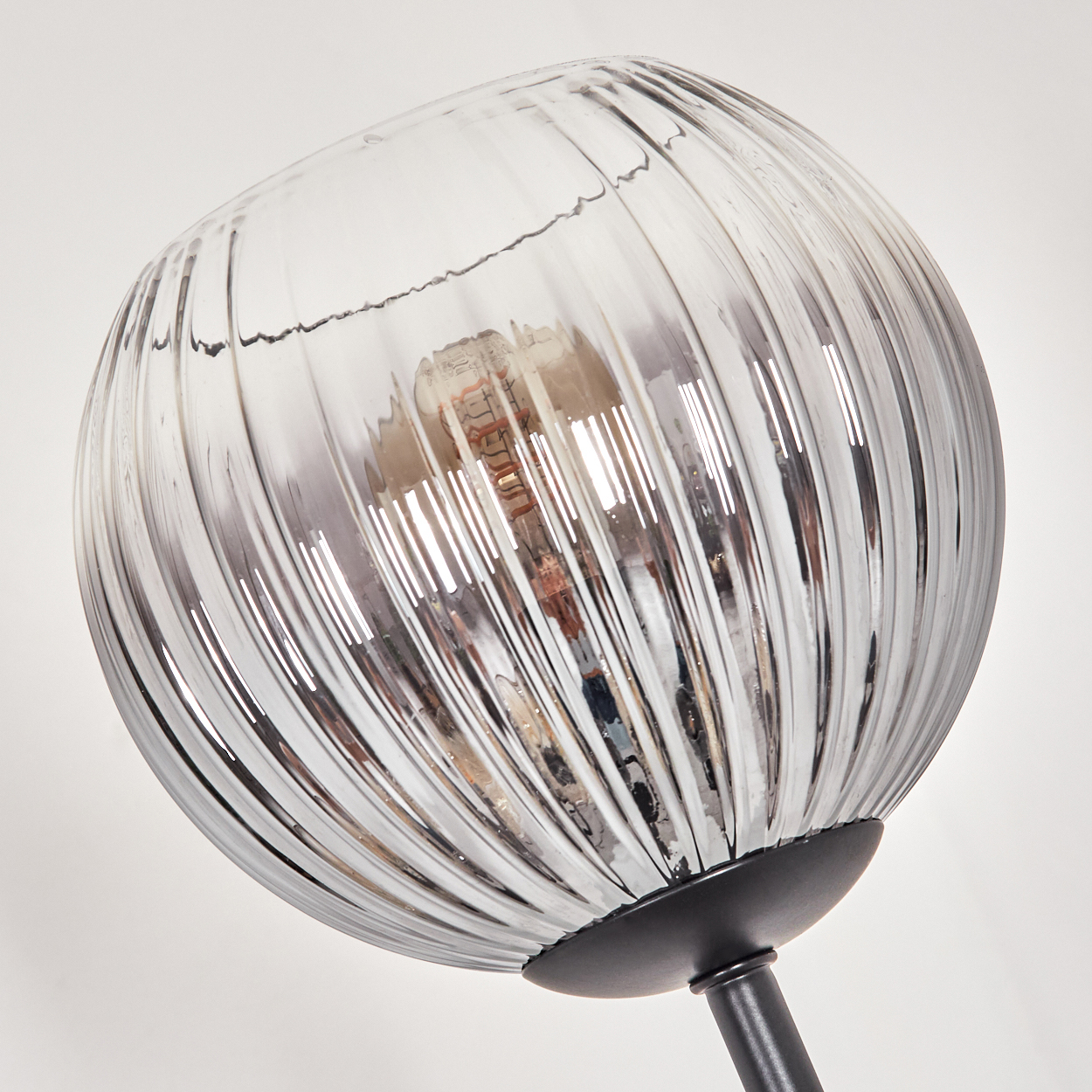 Nahaufnahme einer Glaslampe mit vertikalen Linien. Die Lampe ist klar, mit einer sichtbaren Glühbirne. Der Sockel ist schwarz, der Hintergrund weiß.