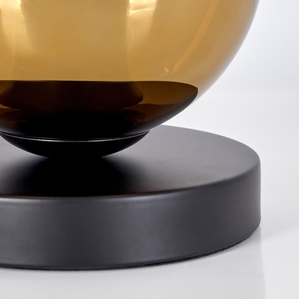 Nahaufnahme einer Lampe. Die Lampe hat einen runden, bernsteinfarbenen Glasschirm auf einem schwarzen, kreisförmigen Sockel.