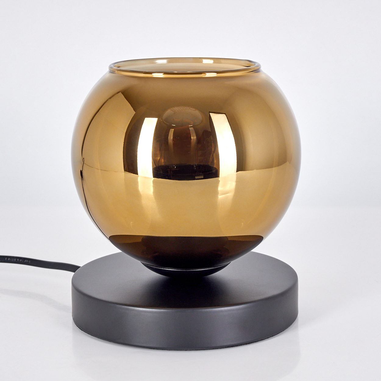 Eine moderne Lampe mit einer goldenen Glaskugel auf einem schwarzen Sockel. Ein schwarzes Kabel erstreckt sich vom Sockel vor weißem Hintergrund.