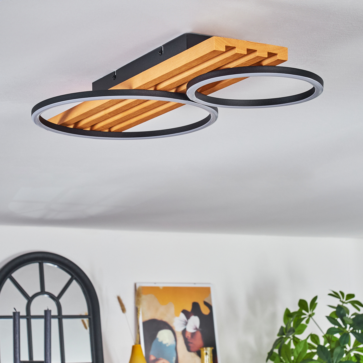 Deckenleuchte mit Holz- und schwarzen Akzenten. Zwei kreisförmige Lichter hängen darunter. Ein Spiegel und Kunst sind im Hintergrund.