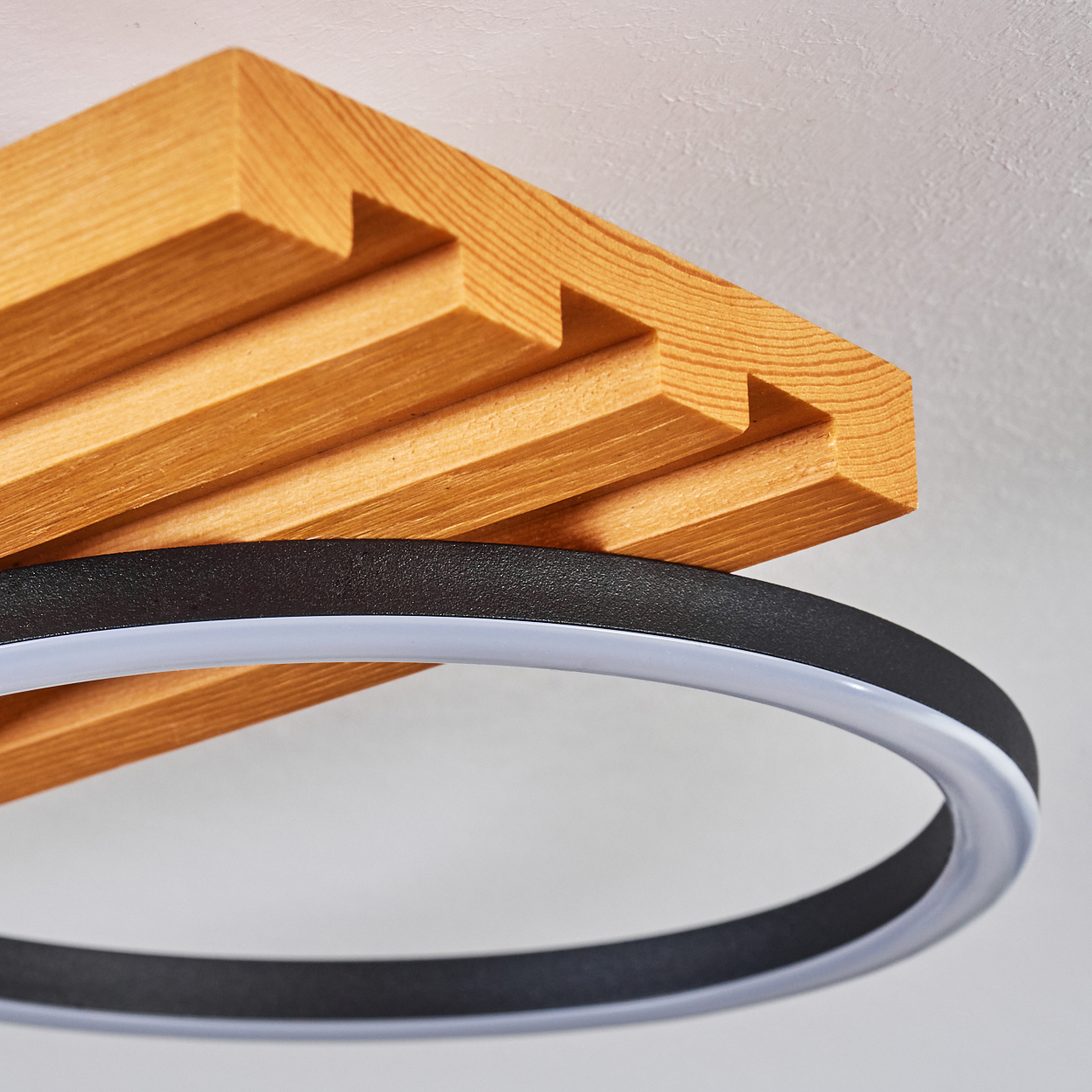 Nahaufnahme einer hölzernen Deckenleuchte. Sie hat einen schwarzen Ring mit weißem Licht und einen Holzbalken.