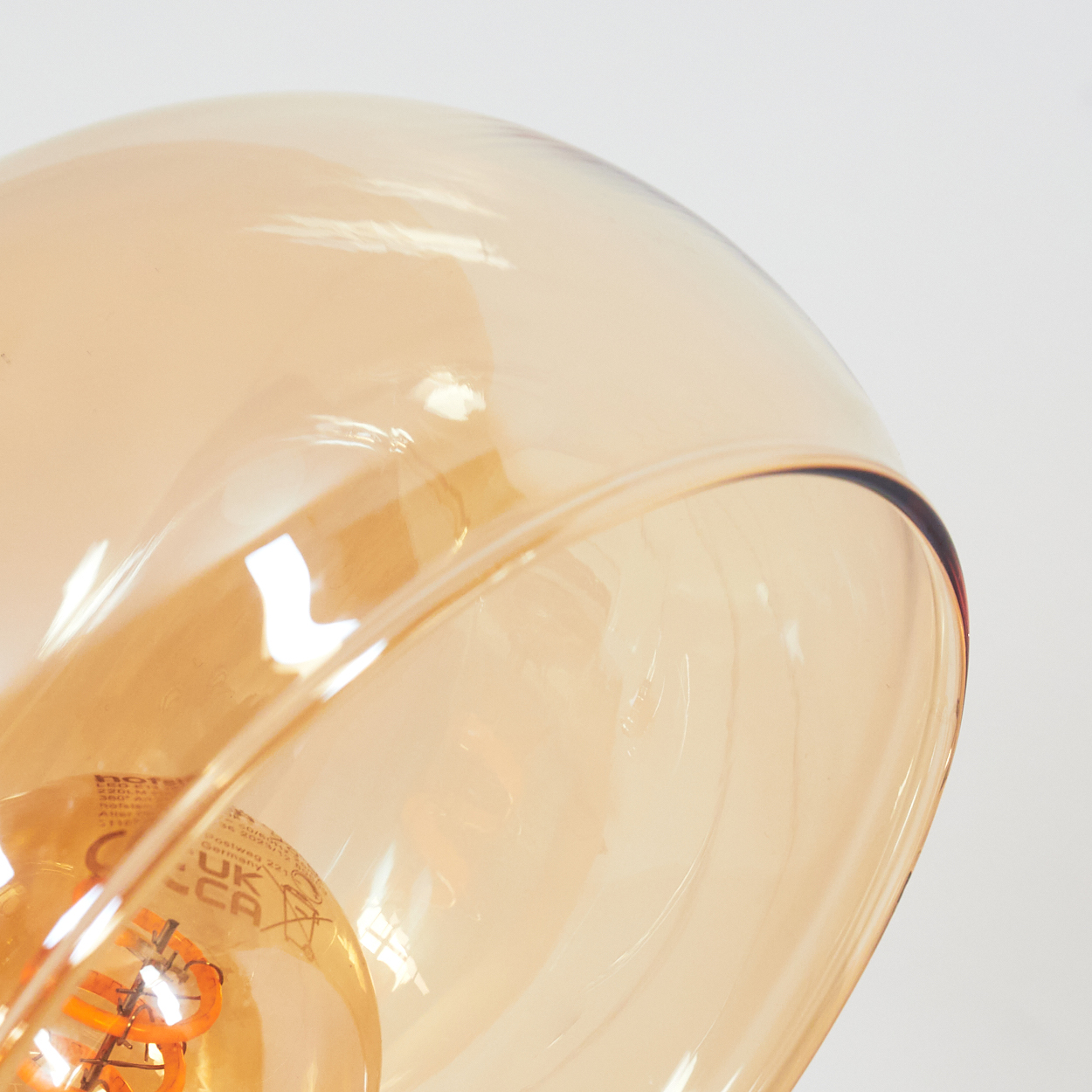 Nahaufnahme eines Lampenschirms aus Glas mit warmem Orangeton und einer sichtbaren Glühbirne. Der Hintergrund ist weiß.