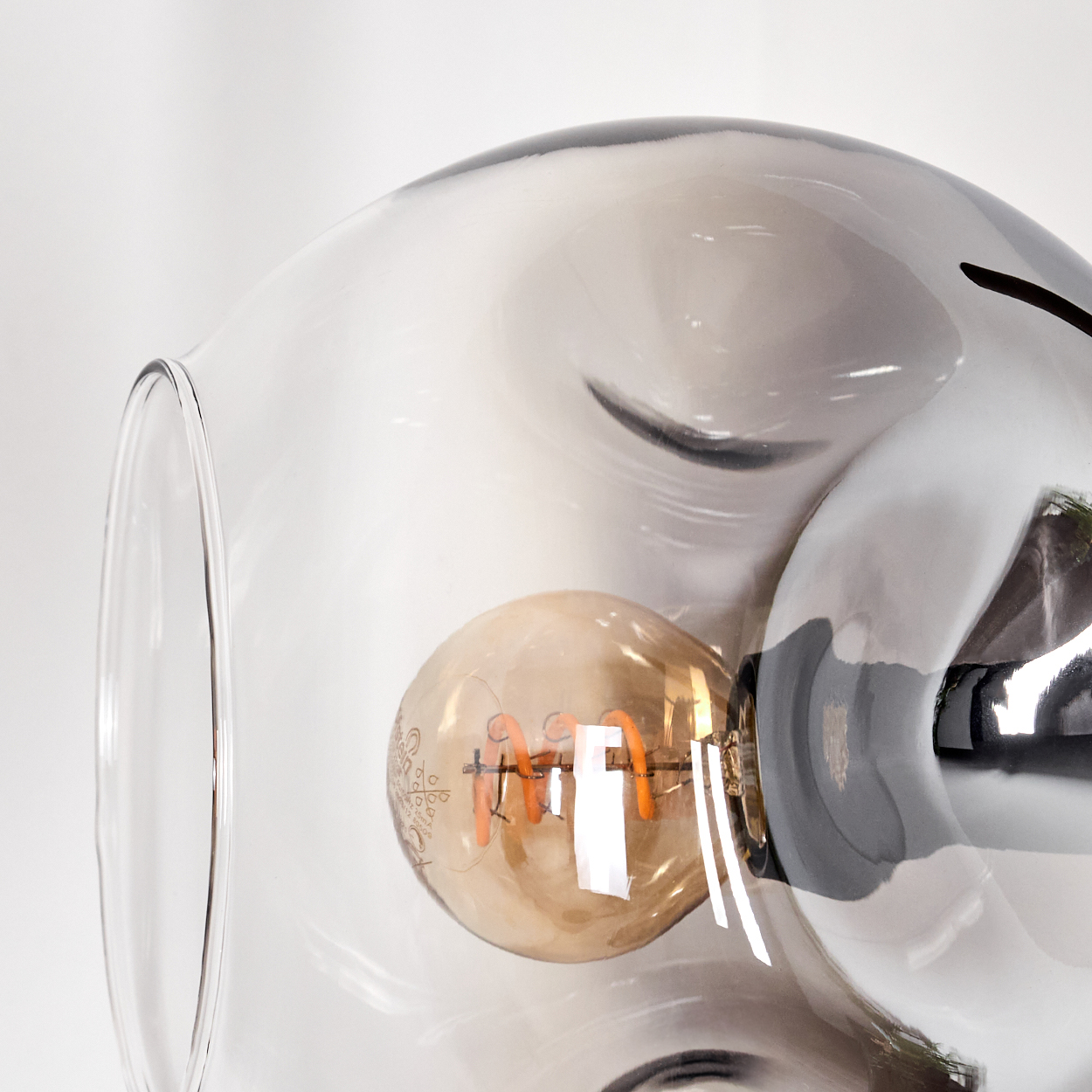 Nahaufnahme einer dekorativen Lampe mit klarem Glasschirm und warmtoniger Glühbirne. Der Hintergrund ist weiß.