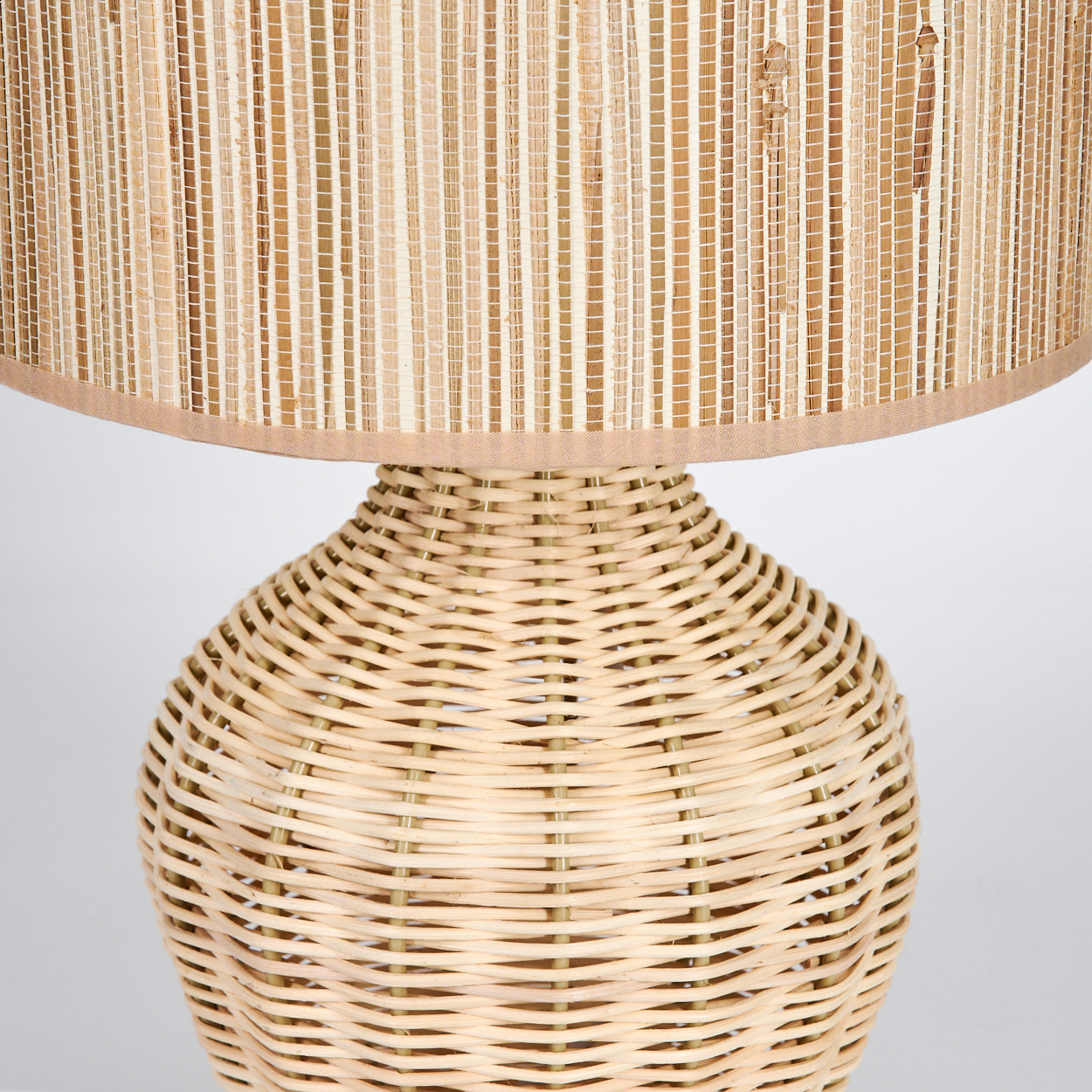 Eine gewebte Lampe mit zylindrischem Schirm und rundem Sockel. Der Schirm ist hell, der Sockel aus gewebtem Material.