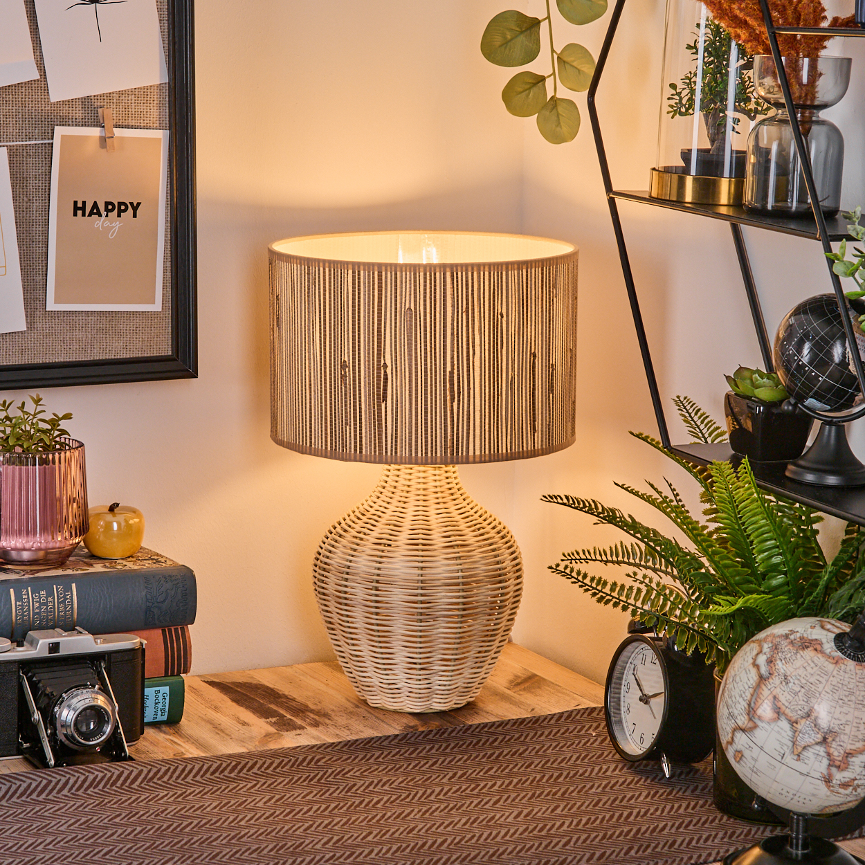 Eine gewebte Lampe steht auf einem Holztisch mit Büchern, einer Kamera und einer Uhr. Eine Pinnwand mit einem 'Happy Day'-Zettel ist sichtbar.