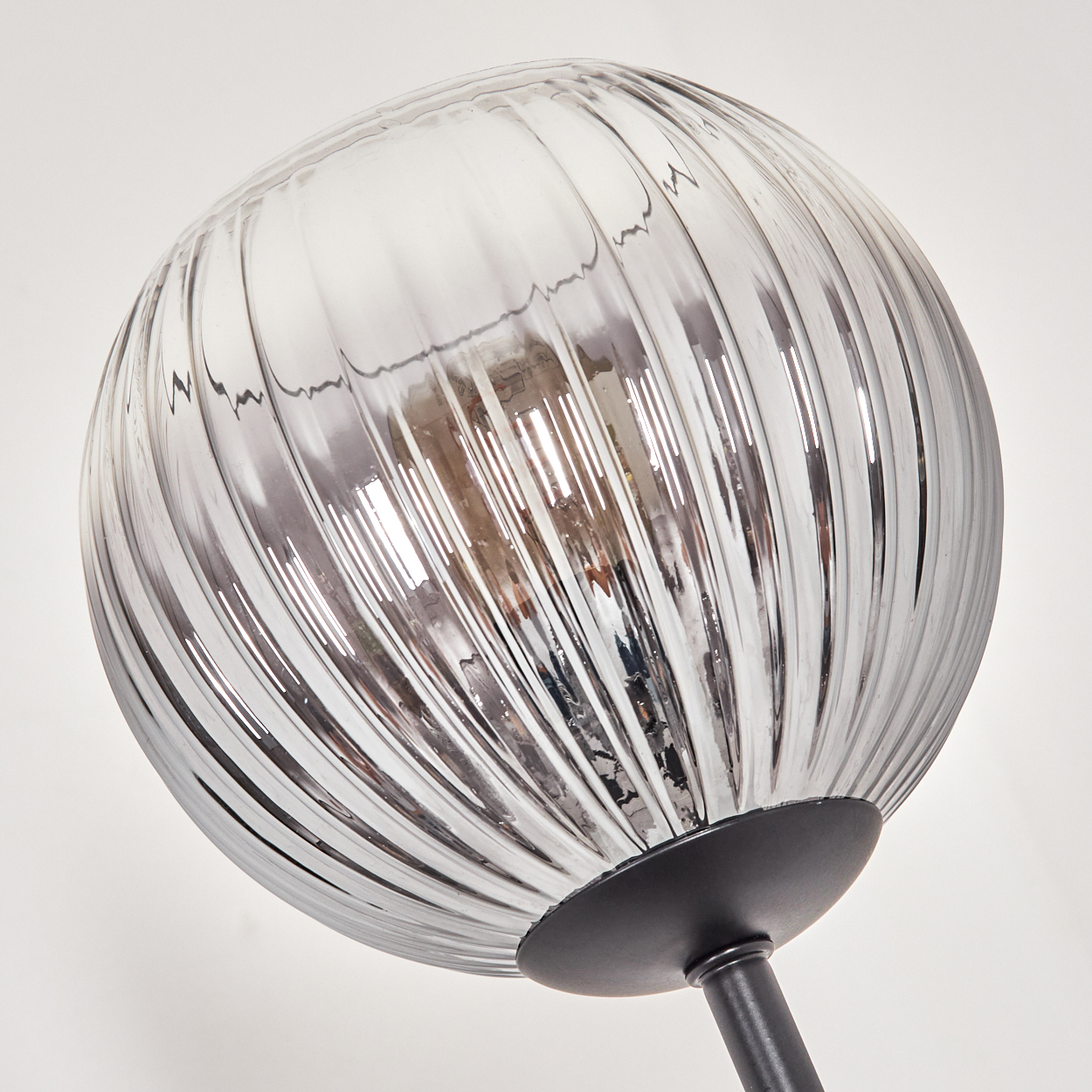 Nahaufnahme einer Glaskugel-Lampe. Die Kugel hat ein geripptes Muster. Sie ist an einem schwarzen Stiel befestigt. Der Hintergrund ist weiß.