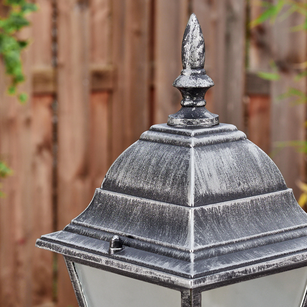 Nahaufnahme einer dekorativen Außenlampe mit silbernem und schwarzem Finish. Ein Holzzaun ist im unscharfen Hintergrund.