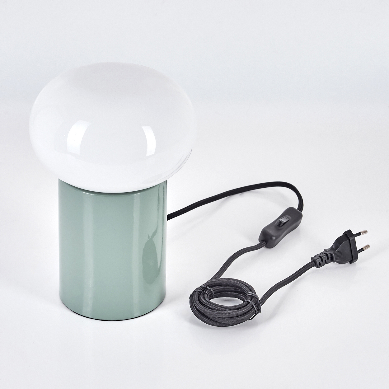 Eine moderne pilzförmige Lampe mit weißem Globusschirm und grünem Sockel. Ein schwarzes Kabel und Stecker sind mit der Lampe verbunden.