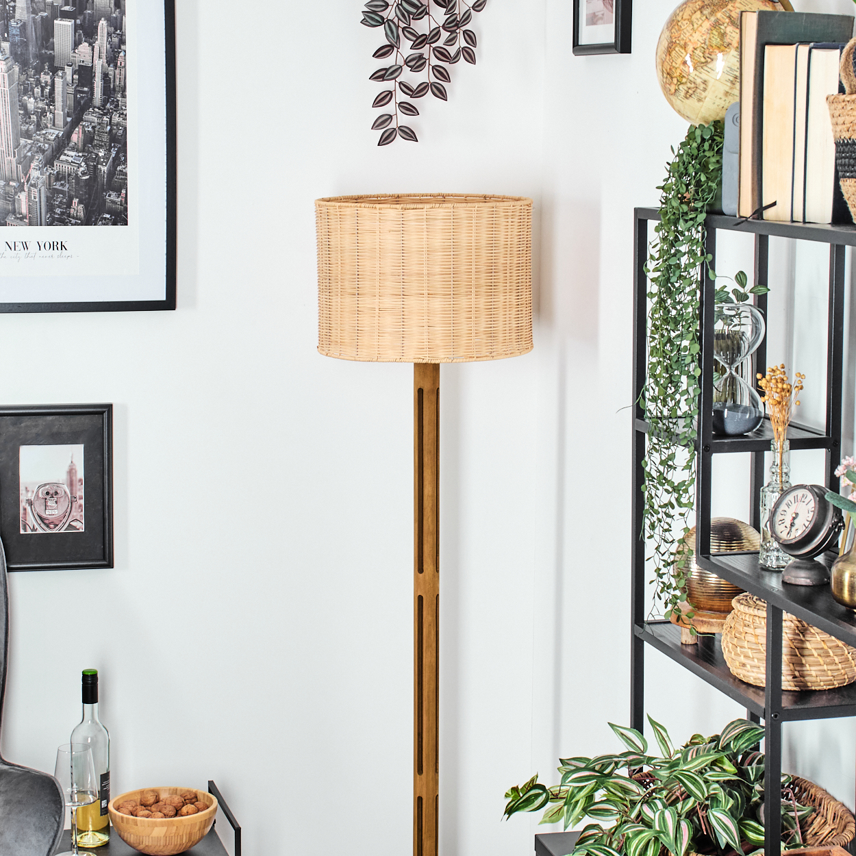 Eine Zimmerecke mit einer gewebten Lampe, schwarz gerahmten Bildern, einem Regal mit Dekoration und einer Schüssel mit Walnüssen.