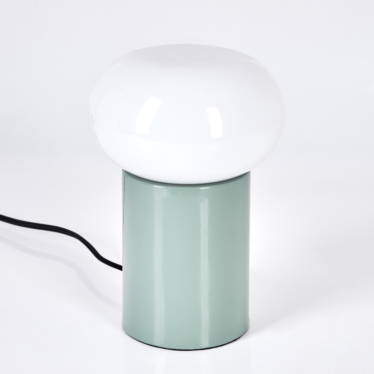 Eine moderne Lampe mit weißem, kugelförmigem Schirm auf einem zylindrischen, hellgrünen Sockel. Ein schwarzes Kabel erstreckt sich.