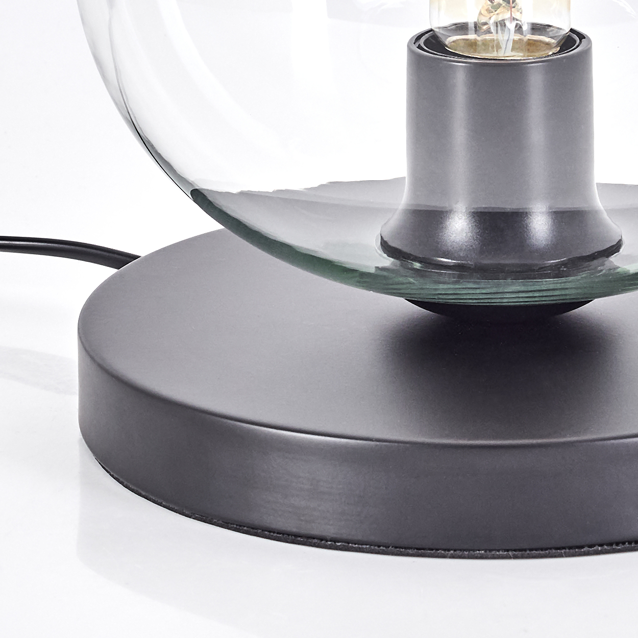 Nahaufnahme einer Lampe mit Glasschirm und schwarzem Sockel. Die Glühbirne ist sichtbar. Der Hintergrund ist weiß.
