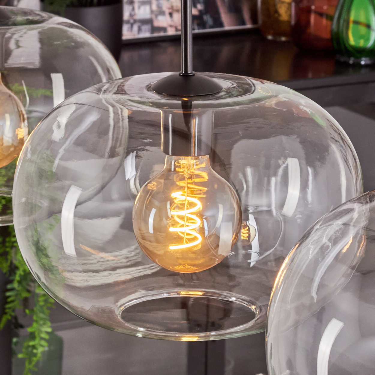 Nahaufnahme einer modernen Leuchte mit klaren Glaskugeln und Edison-Glühbirnen, warmer Beleuchtung und dunklem Hintergrund.