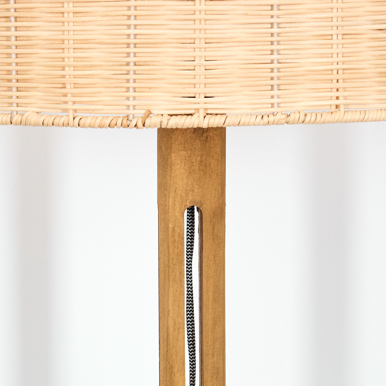 Nahaufnahme einer Lampe mit gewebtem Lampenschirm und Holzständer. Ein schwarz-weißes Kabel verläuft in der Mitte des Ständers.