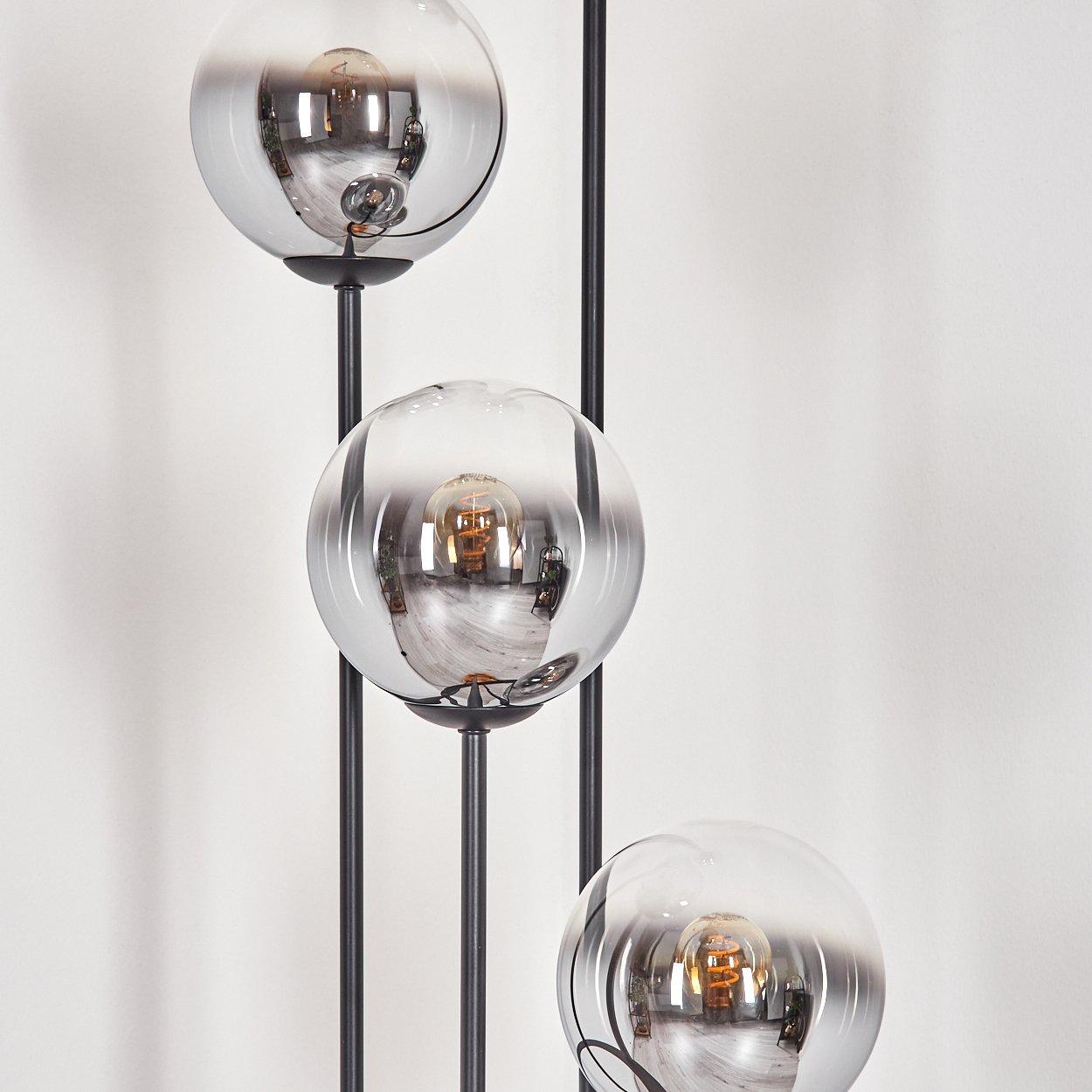Eine moderne Lampe mit drei kugelförmigen, verspiegelten Glasschirmen, jeweils mit einer sichtbaren Glühbirne, vor einer weißen Wand.