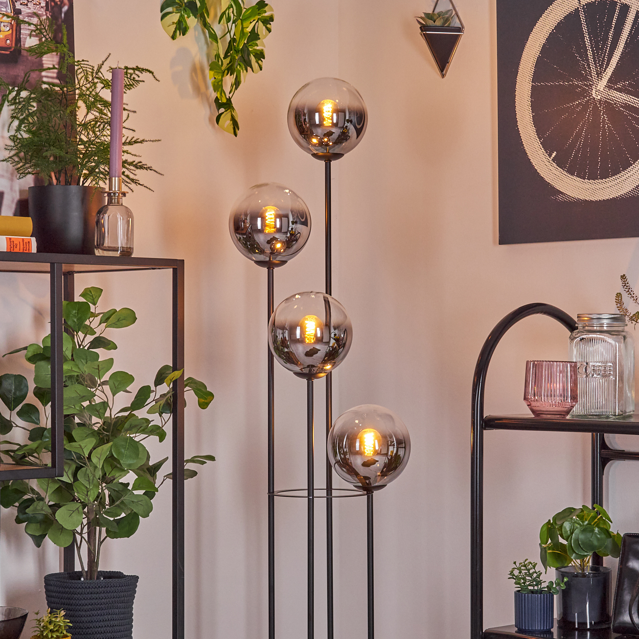 Modernes Wohnzimmer mit Stehlampe mit vier leuchtenden Kugeln. Pflanzen und Regale mit Dekoration vor einer beigefarbenen Wand.