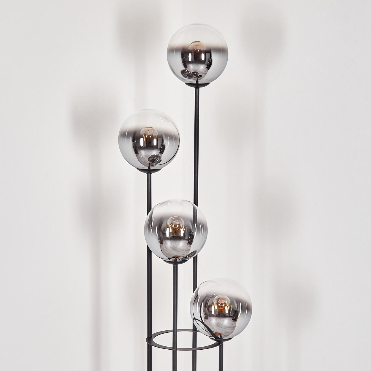 Eine moderne Stehlampe mit vier kugelförmigen, verspiegelten Glasschirmen, jede mit einer sichtbaren Glühbirne, auf einem schwarzen Metallrahmen.
