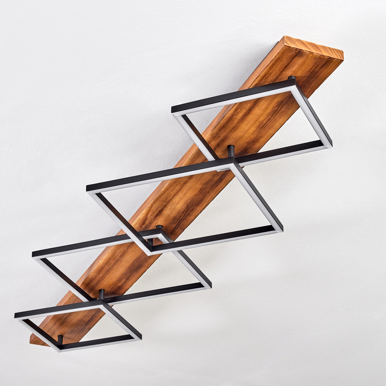 Ein modernes Holzregal mit schwarzen und silbernen quadratischen Rahmen vor einer weißen Wand. Das Regal hat ein Zickzackmuster.