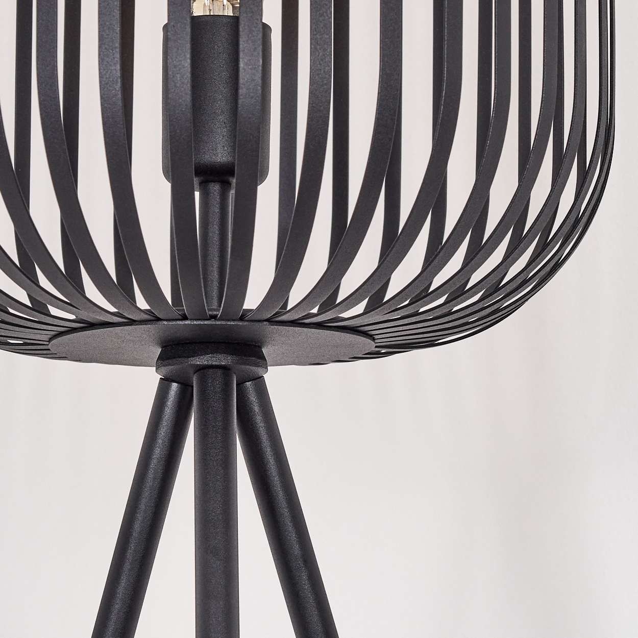 Nahaufnahme einer schwarzen Metalllampe. Die Lampe hat einen käfigartigen Schirm und ein Stativ. Der Hintergrund ist weiß.
