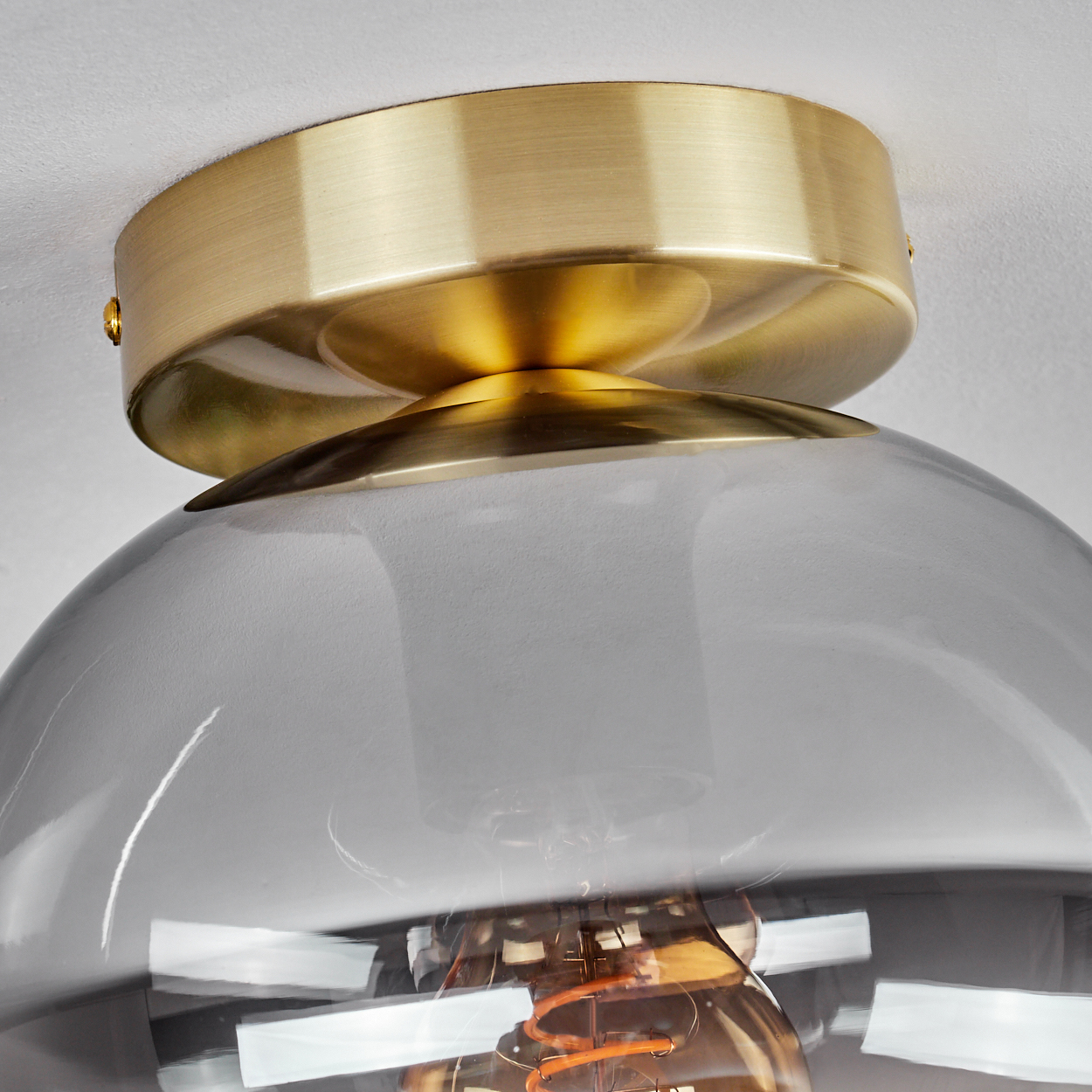Nahaufnahme einer Deckenleuchte mit goldfarbenem Sockel und rauchgrauem Glasschirm, der eine sichtbare Glühbirne zeigt.