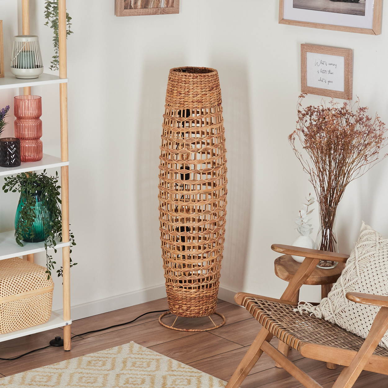 Eine gewebte Stehlampe aus Rattan steht neben einem Holzstuhl. Ein Regal mit Dekoration und ein Teppich sind ebenfalls vorhanden.