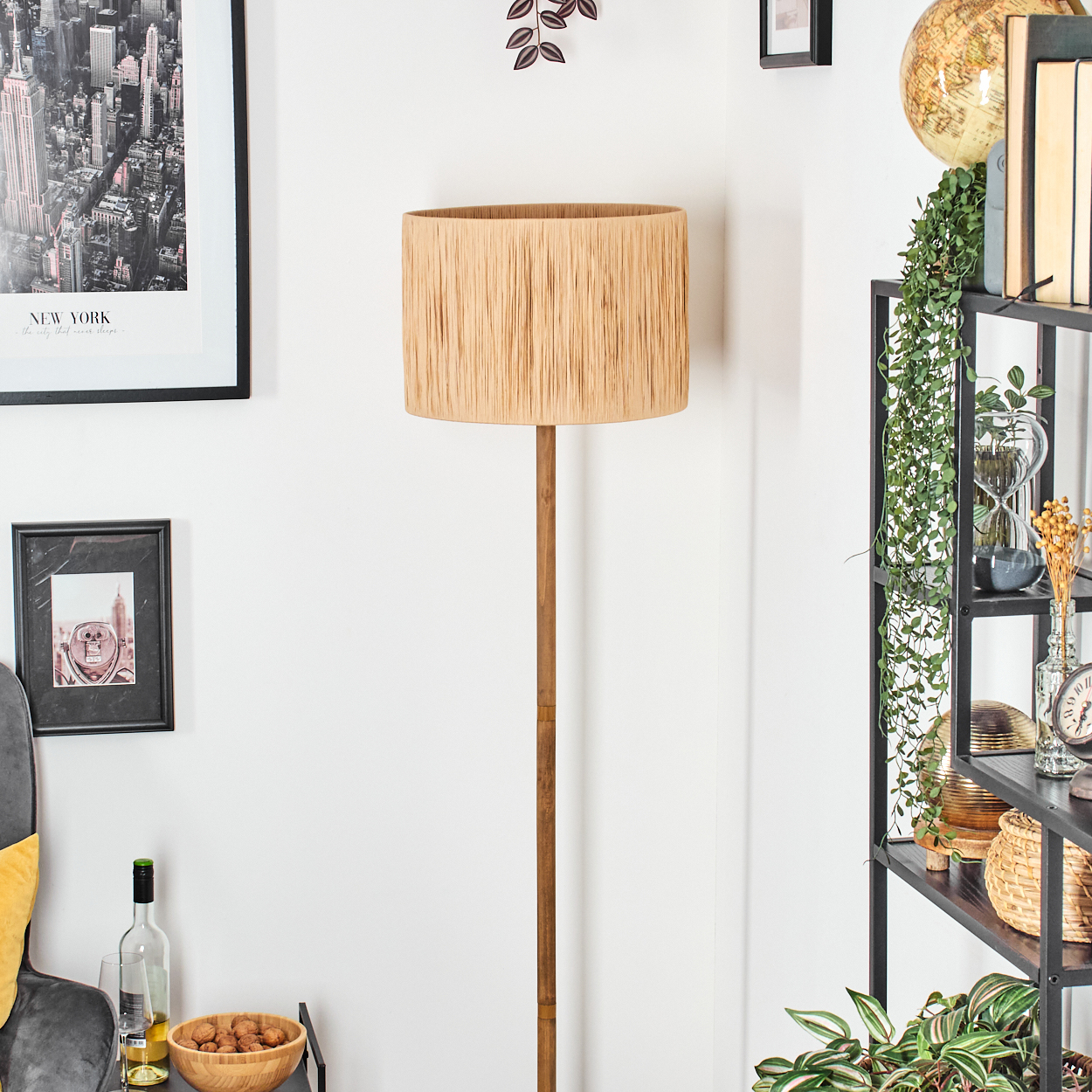 Ein Raum mit einer Stehlampe. Rechts ein Regal mit Dekoration. Links Bilder und eine Schüssel mit Nüssen.