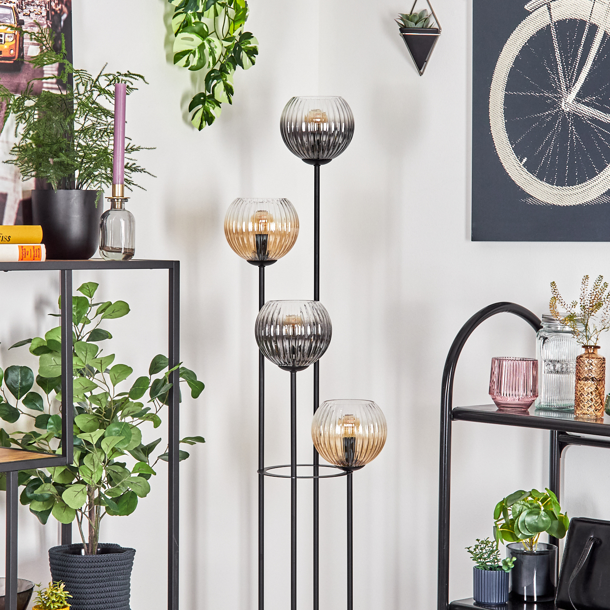 Ein modernes Wohnzimmer mit einer schwarzen Metalllampe mit Glasschirmen, Pflanzen, Regalen und einem Fahrradrad-Kunstwerk.