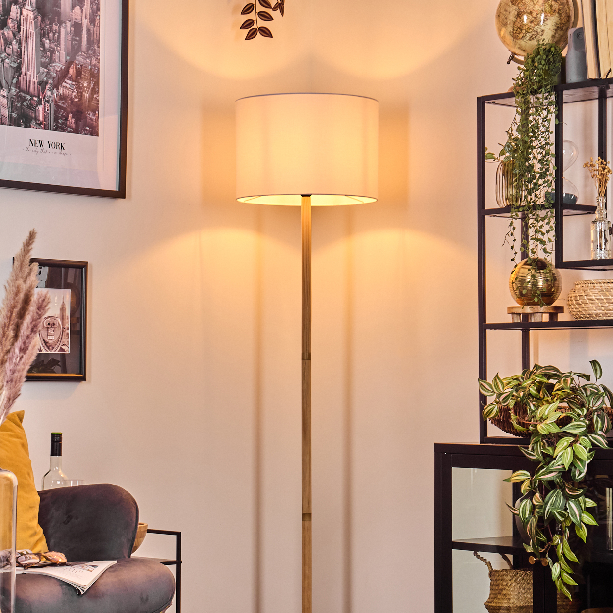 Eine Stehlampe steht in einem Raum mit einem schwarzen Regal voller Pflanzen und Dekoration. Ein New York-Poster hängt an der Wand.