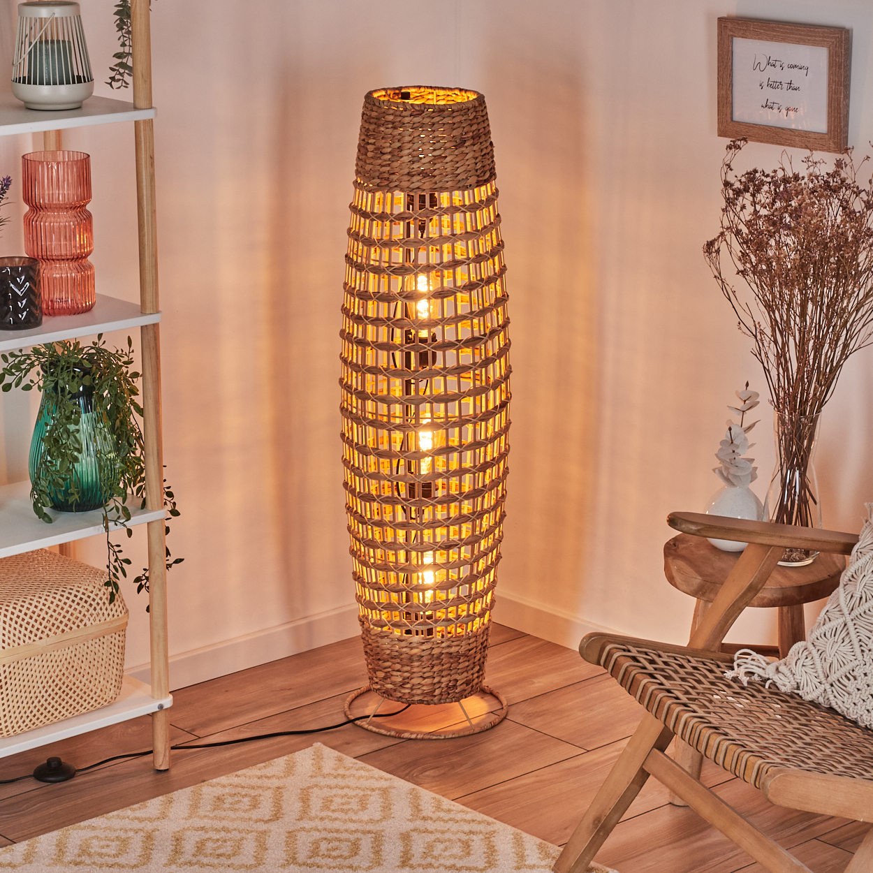 Eine gewebte Lampe leuchtet neben einem Stuhl und einem Regal mit Dekorationsartikeln. Der Raum hat warme Beleuchtung und einen Teppich.